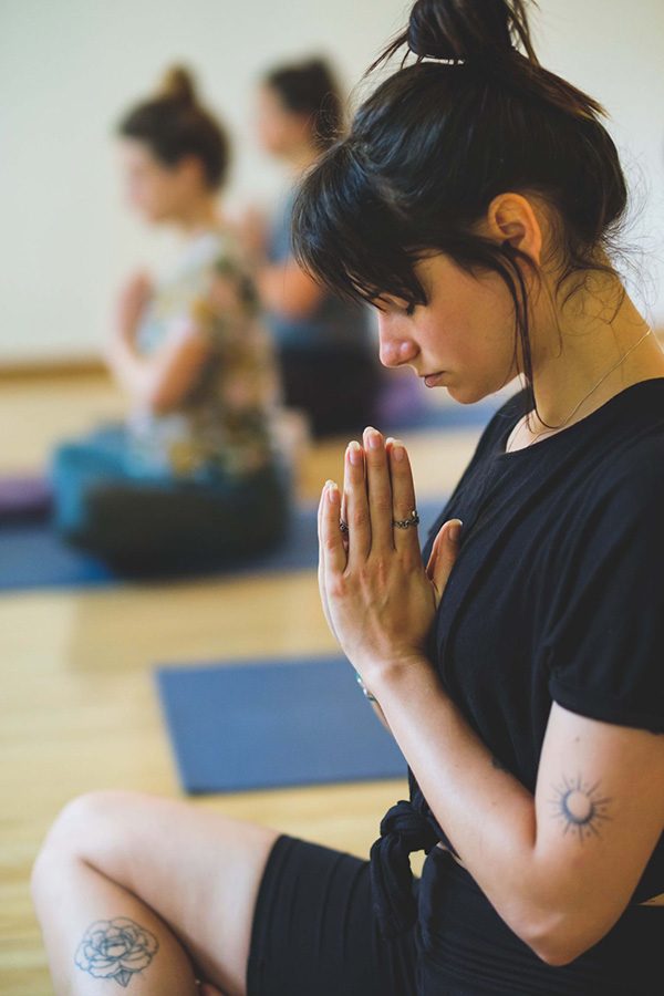 A woman sitting on a mat with her eyes closed and hands together, practicing mindfulness or meditation.